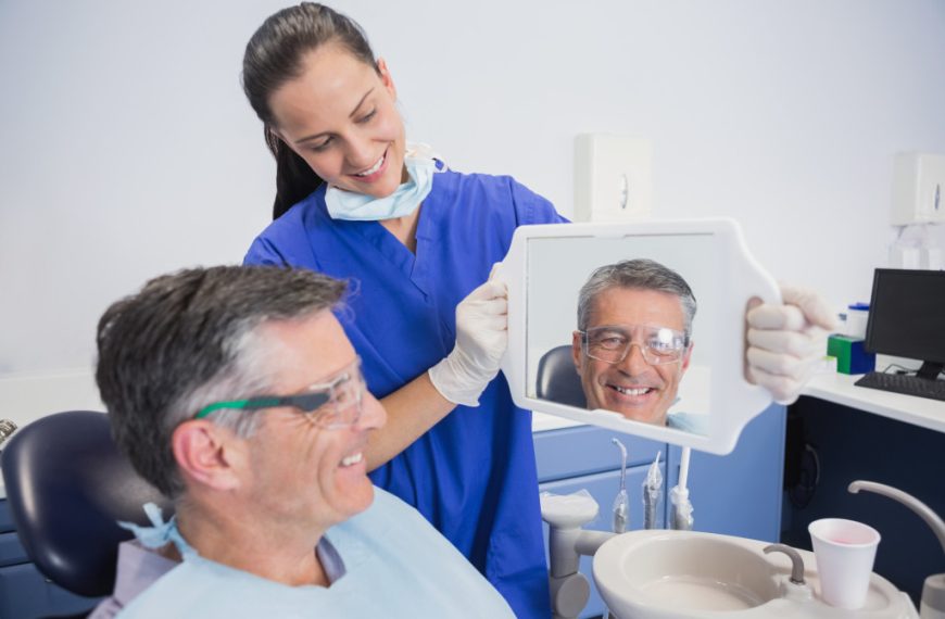 a senior man in a dental clinic looking at a mirror held by a nurse