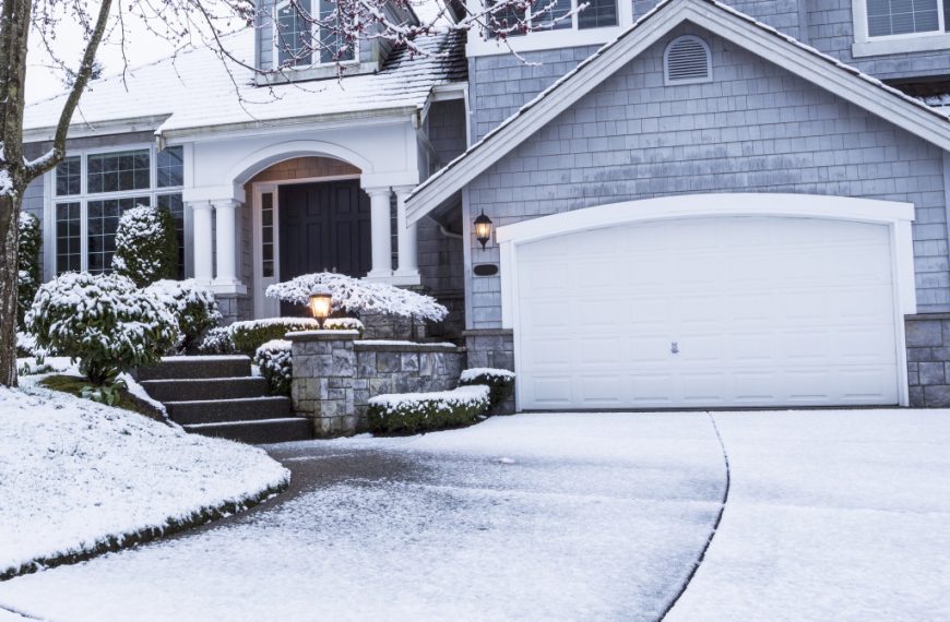 suburban home with snow on driveway and lawn