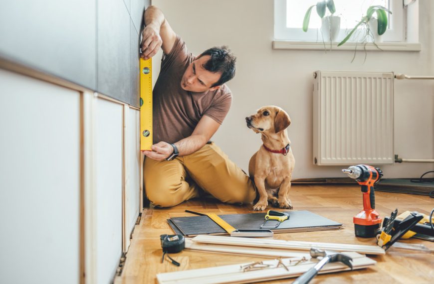 a man measuring a wall to renovate with a dog beside him