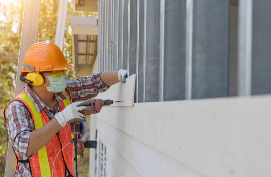 Worker installing wall panels while wearing protective gear.