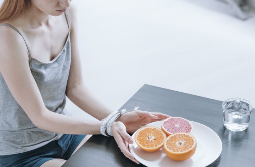 Restrictive diet concept. A girl being kept from eating fruits on a plate with measuring tape tied to her wrists