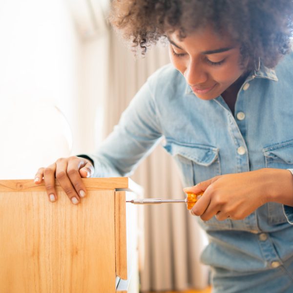 smiling curly haired woman repairing a broken cabinet with screwdriver
