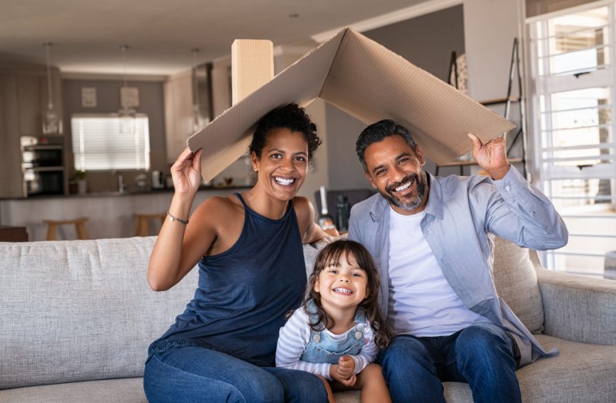 A young family holding a cardboard as a roof in their living room