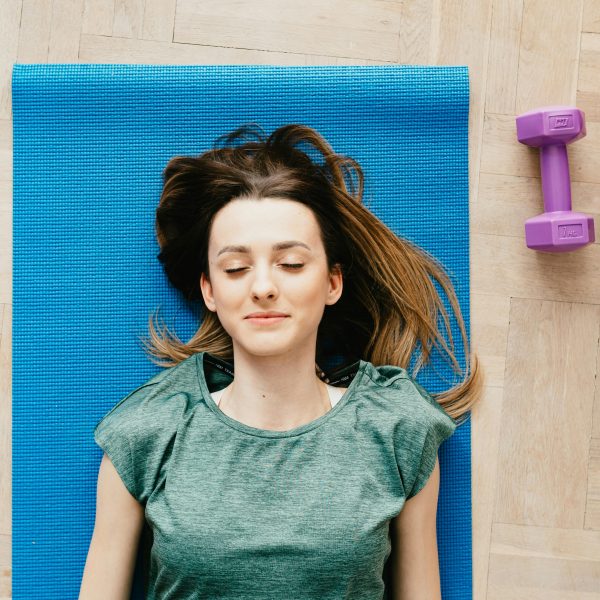 woman lying on a blue yoga mat, meditating with dumbbells beside her