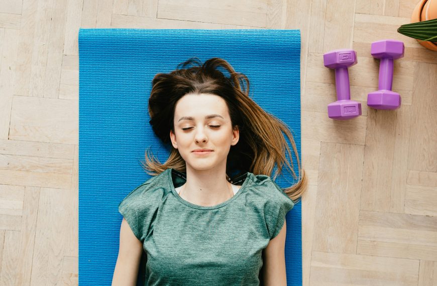 woman lying on a blue yoga mat, meditating with dumbbells beside her